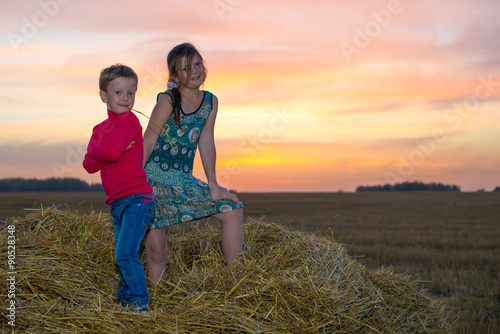 Boy and girl standing on a stack of straw yellow smiling on the background of the setting  the rising sun in the clouds