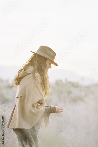 A woman in a warm coat and a hat picking wild flowers.