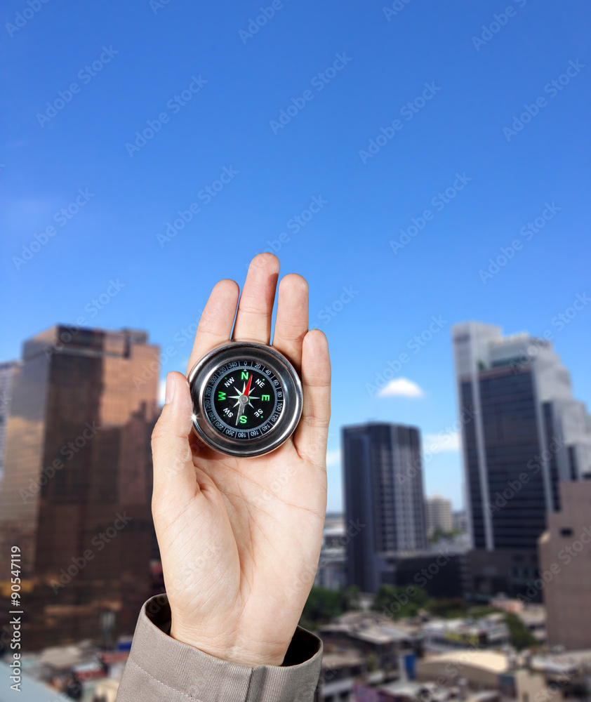 Business direction, Hand holding a magnetic compass over a city buildings