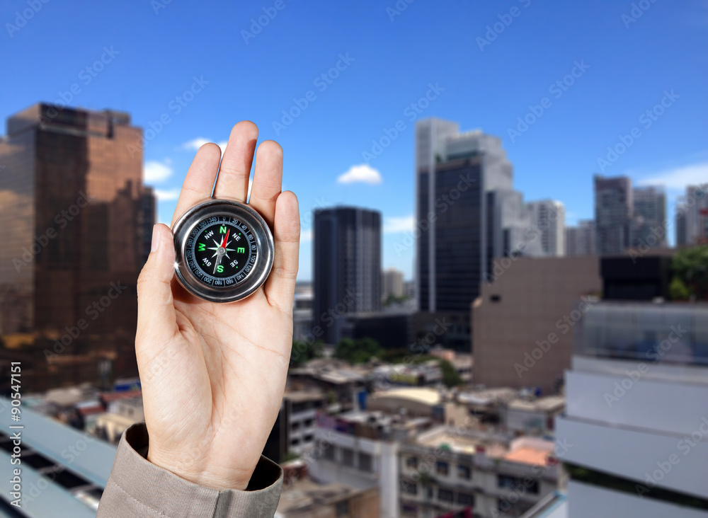 Business direction, Hand holding a magnetic compass over a city buildings