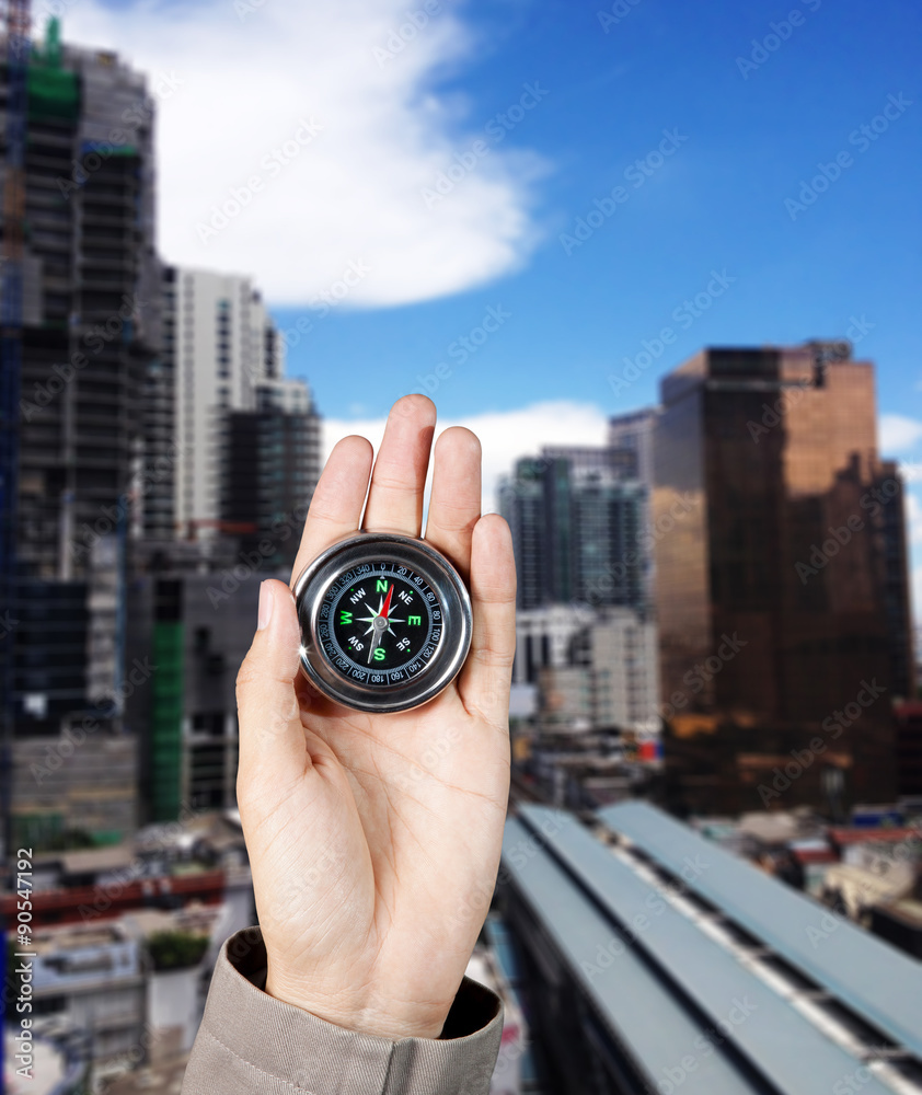 Business direction, Hand holding a magnetic compass over a city buildings