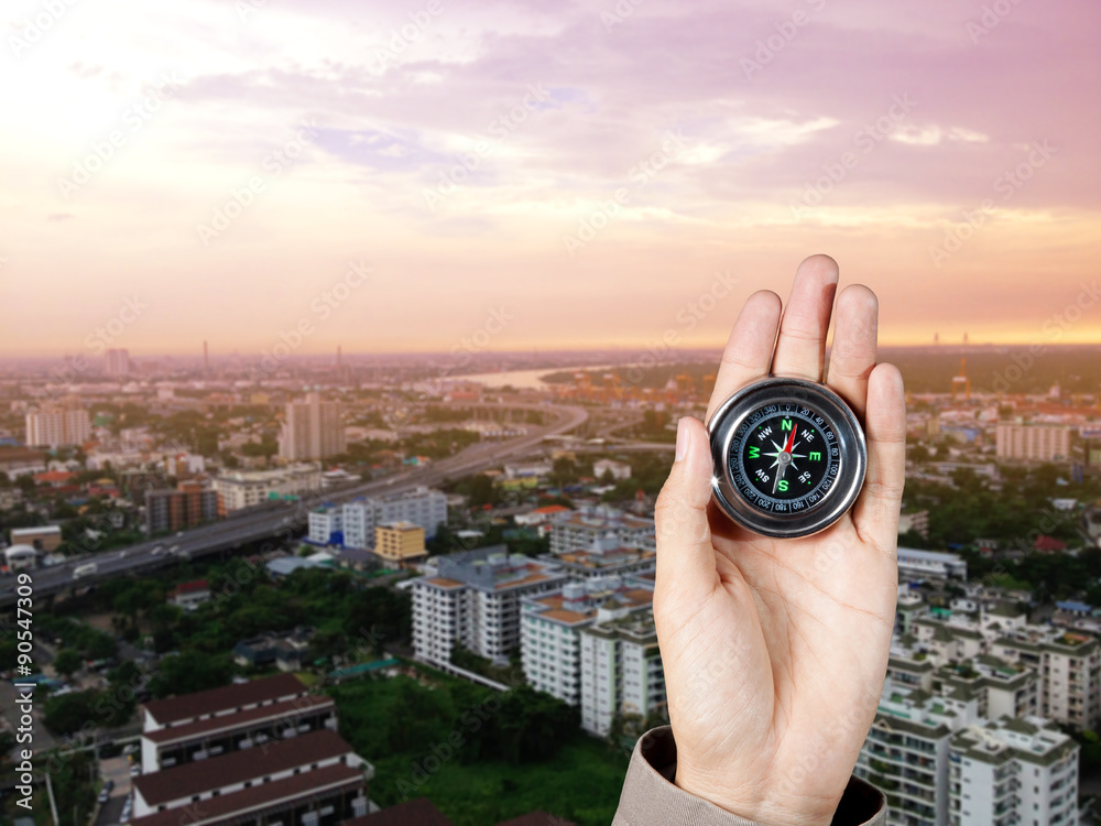 Business direction, Hand holding a magnetic compass over a city buildings