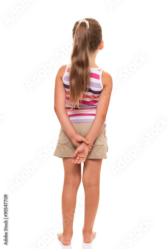 A little girl stands back, holding her hands behind her back