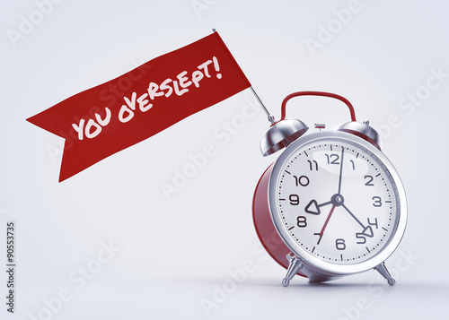 You Overslept! Alarm clock with a red banner and written phrase on it. 3D rendered graphics on light background. The text on the banner created with the Permanent Marker font under Apache License V2.0 © Sergey Tarasov