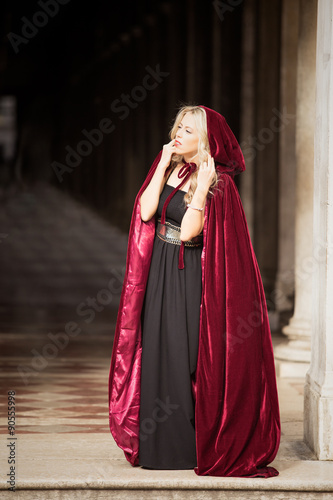 Mysterious woman in red cloak standing in dark arch