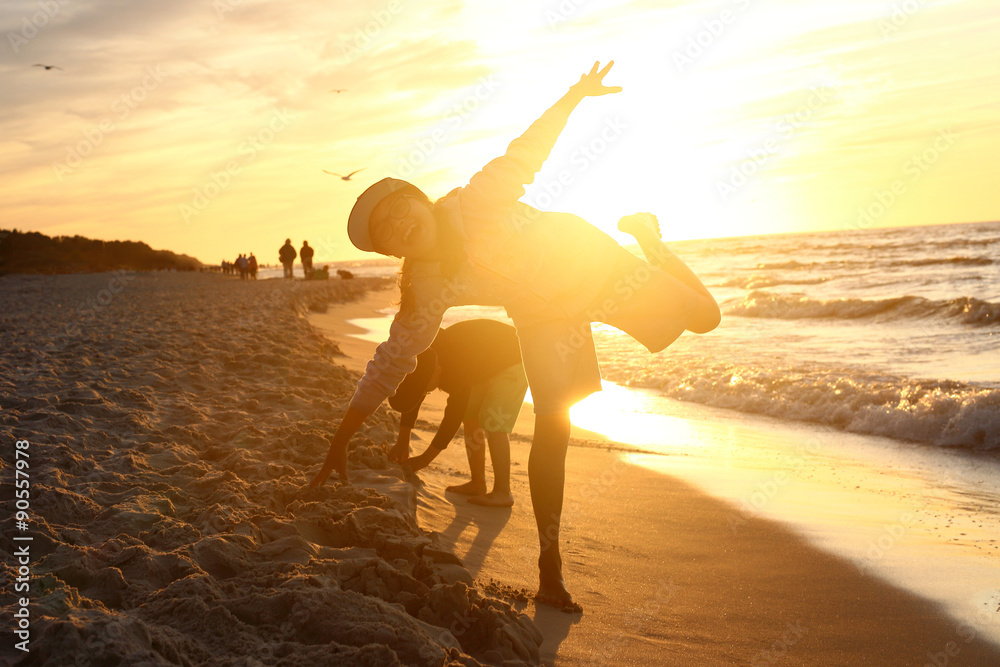 Zabawa przy zachodzie słońca. Dzieci chłopiec i dziewczynka bawią się na brzegu morza podczas zachodu słońca - obrazy, fototapety, plakaty 