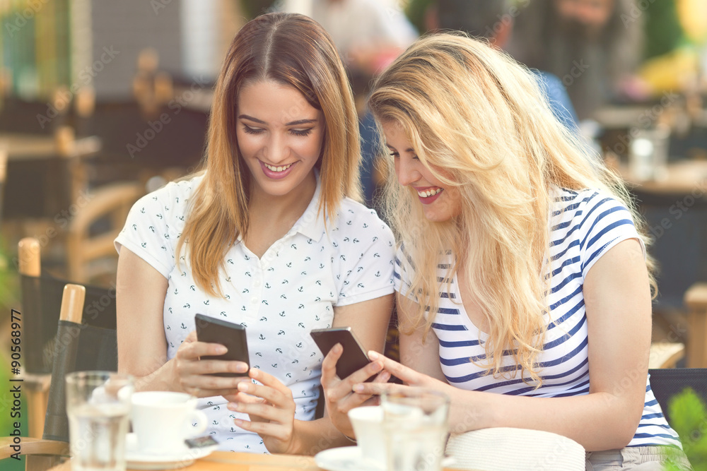 Two young women using mobile phones while relaxing in a cafe