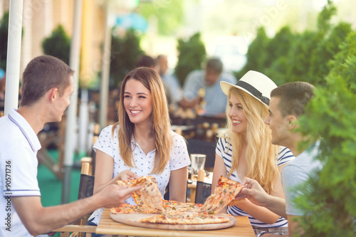Four cheerful young friends sharing pizza in a outdoor cafe