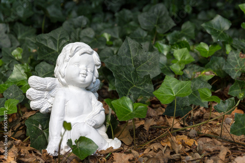 Wei  e Engelfigur sitzt vor Efeu im Garten
