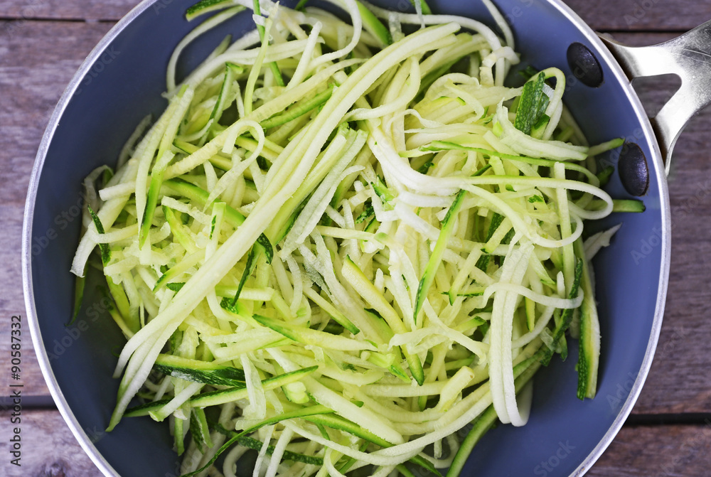 Grated zucchini and squash in pan on wooden table close up