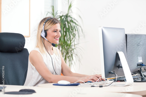 Portrait of smiling young woman working on a computer in a call center photo