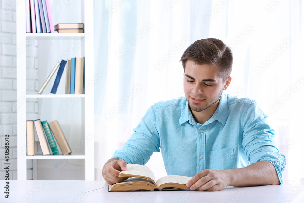 Young man reading book at table in room Young man reading book at table in room