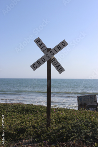 Rail Road Crossing Sign with Ocean and Blue Sky Background