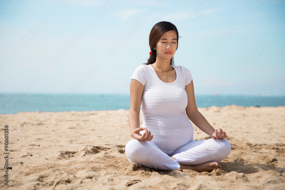 Pregnant asian woman doing yoga in the sea shore