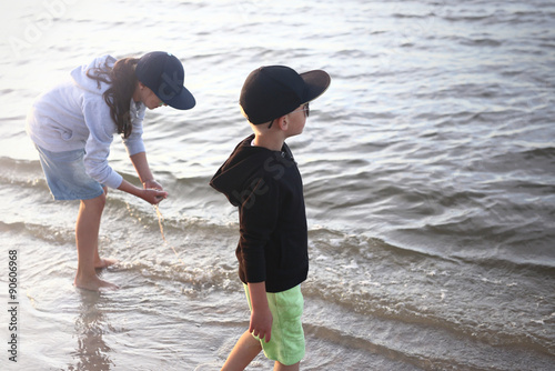Wakacje nad morzem. Dzieci chłopiec i dziewczynka bawią się na brzegu morza wyławiając z wody meduzy