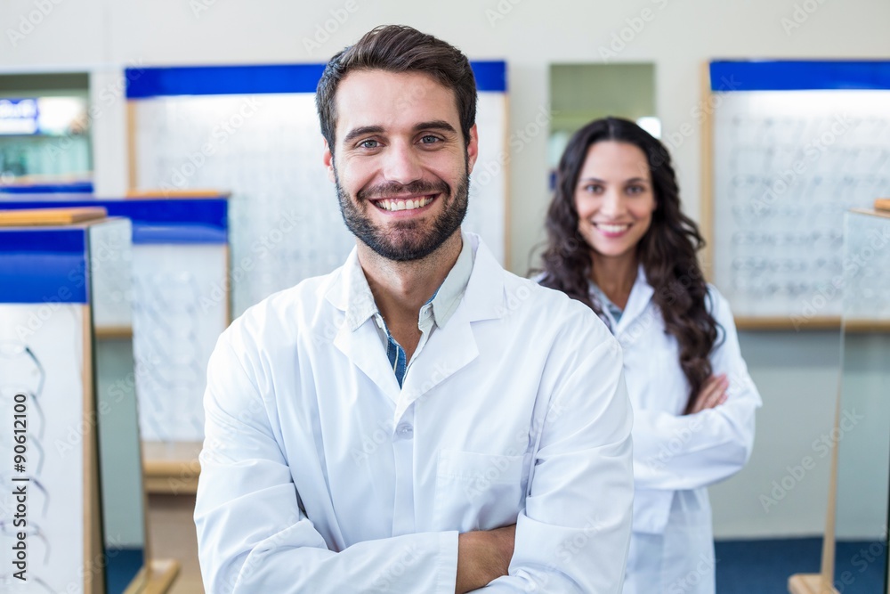A male optician arm crossed with his colleague behind him A male optician arm crossed with his colleague behind him