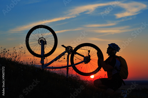 silhouette of man cyclist repairing a bike against sunset