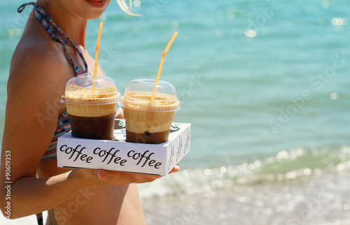 Attractive female waiters holding two ice frappe coffee on the beach near sea. Young woman enjoyng during summer holiday, vacation  on tropical resort by ocean. Sunset colors. photo