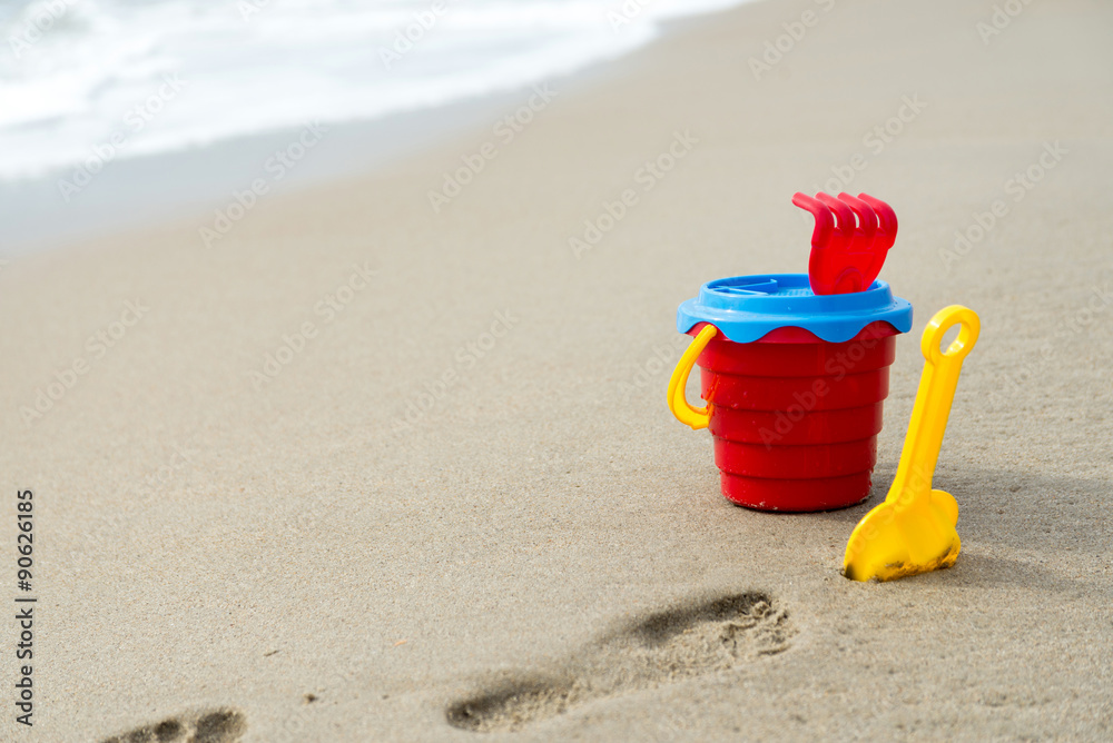 Red bucket with a shovel, a rake and a net on the beach and wet sand Red bucket with a shovel, a rake and a net on the beach and wet sand