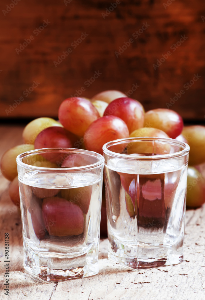 Grappa in a small glass and ripe grapes on old wooden table, sel Grappa in a small glass and ripe grapes on old wooden table, sel