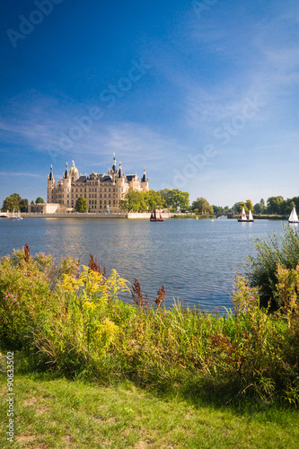 Schweriner Schloss spiegelt sich im See mit einigen Segelbooten