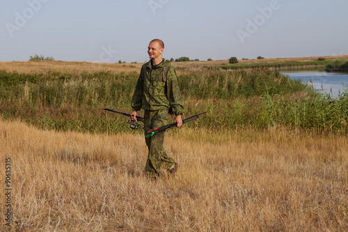 man with a fishing rod in camouflage suit is in the field