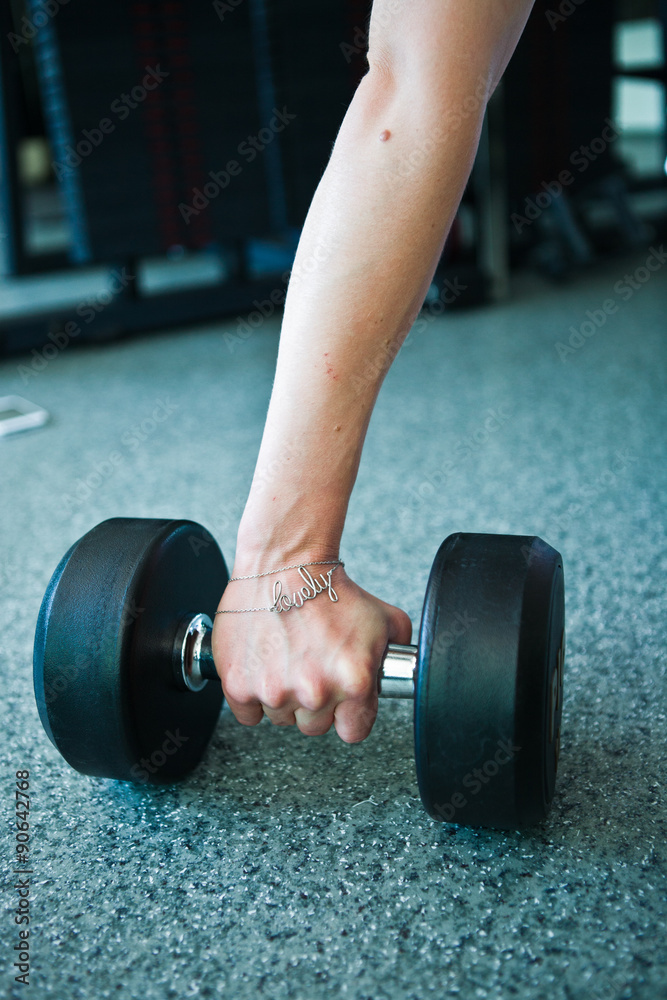 female hand taking dumbells from row of barbells in gym
