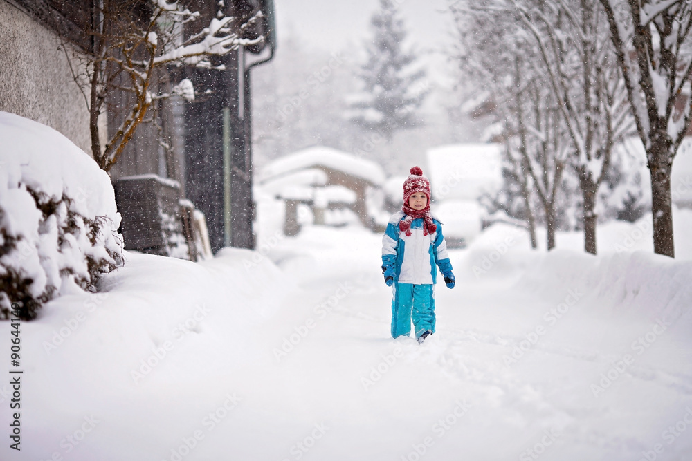 little boy in a snowsuit walking through a snowy path with deep