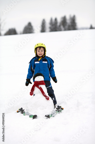 Happy little boy playing in the snow while snowing, helmet