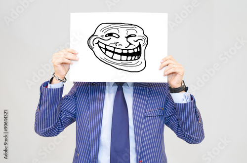 Business man hoding card with troll face on grey background