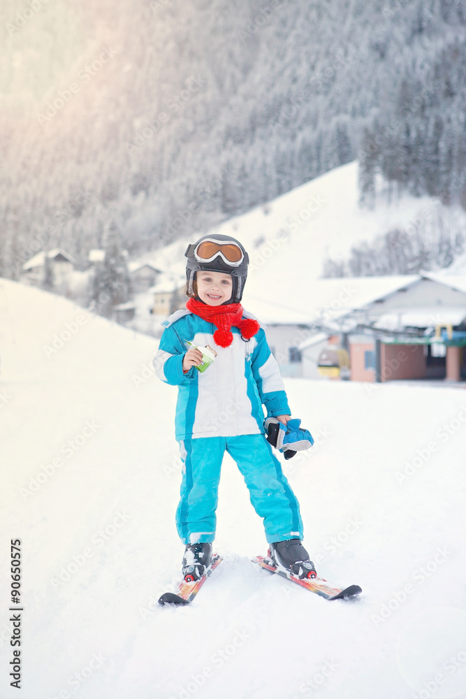Adorable little boy with blue jacket and a helmet, skiing
