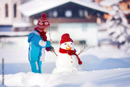 Happy beautiful child building snowman in garden, winter photo