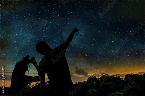 Silhouette of adult man observes night sky with child.