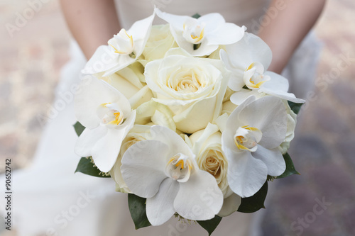 White wedding bouquet of roses and orchids in the hands of the bride