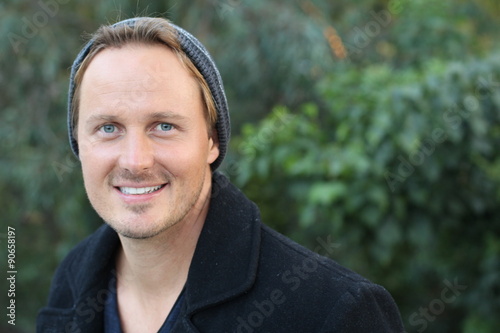 Portrait of a smiling young man in warm clothing shivering while having a walk in forest on a winter day