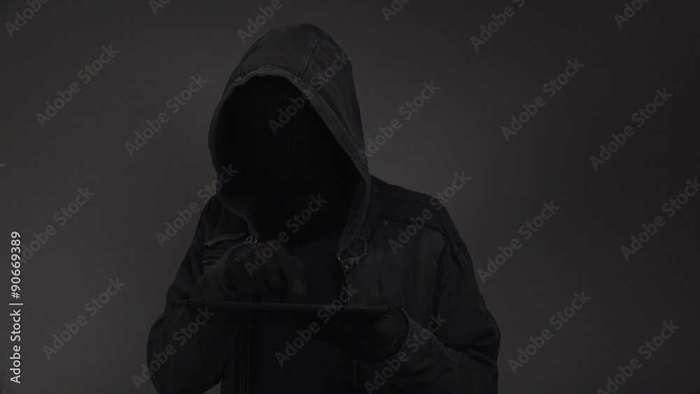 Hooded cyber criminal using digital tablet computer to access deep web internet page, p2p, piracy or network security concept, 4k uhd footage