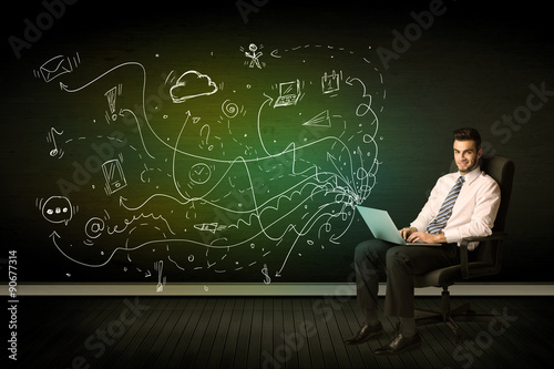 Businessman sitting in chair holding laptop with media icons