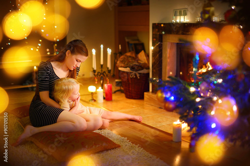 Young mother and daughter sitting by a fireplace on Christmas