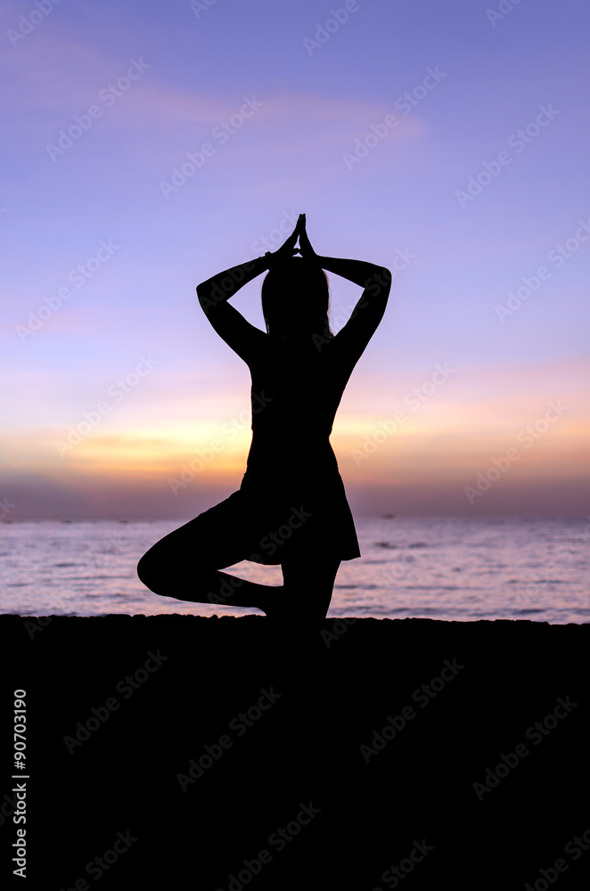 Silhouette young woman practicing yoga on the beach at sunset.