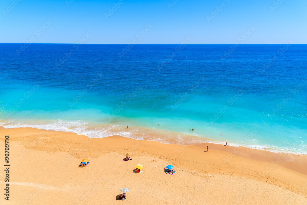 Sun umbrellas and people swimming in ocean on sandy Benagil beach, Portugal