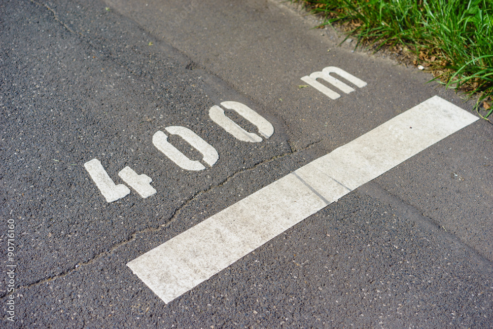Fototapeta premium Auf dem rissigen, sonnengetrockneten Asphalt verewigt sich das Ziel vieler in großen dick aufgetragenen Lettern: 400 m.