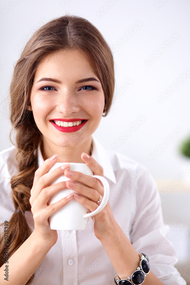 Young businesswoman sitting on the desk with cup in office Young businesswoman sitting on the desk with cup in office