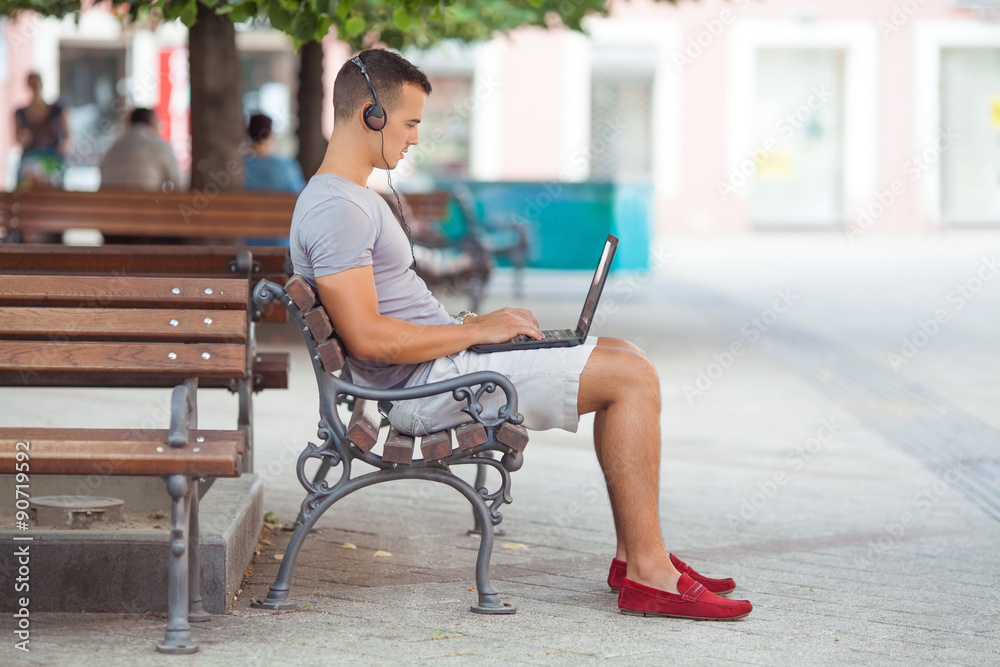 Busy young businessman working on his laptop while sitting on the park bench