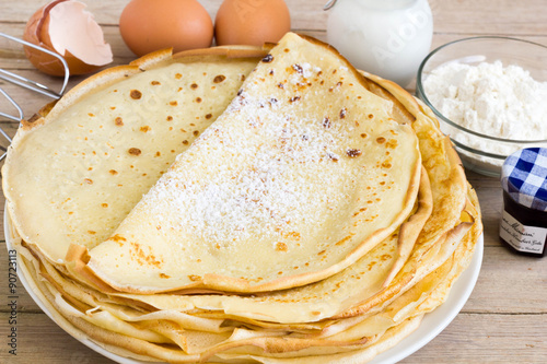 Crepes on each other with ingredients on the table.