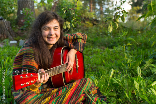 Young girl with an acoustic guitar sitting in the grass.