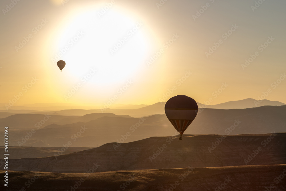 Two ballons in front of big sun over mointains and rocks in cappadocia