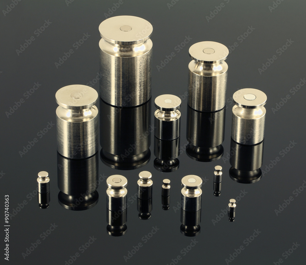 Set of iron weights on light (almost white) surface with chessboard background. Hemi-transparent surface shows chess board background. 