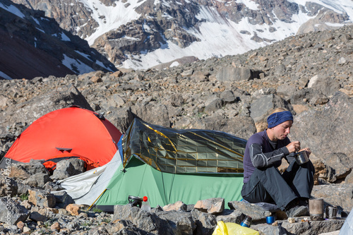 Female Climber Eating Ascetic Breakfast Mountain Expedition Camp Green and Red Tents Woman Sitting and Eating Meal Drinking Tea Steep Rocky and Ice Wall on Background photo