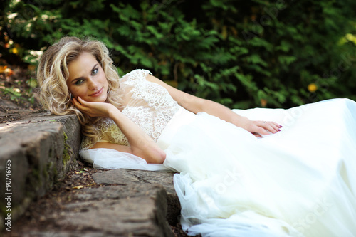 Beautiful bride posing outdoor. Wedding dress, curly blond hair. © MaxFrost