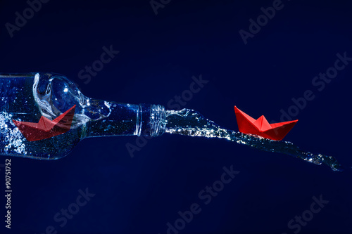 Принти на полотні Red paper boats escape on a water splash from a bottle, dark blu